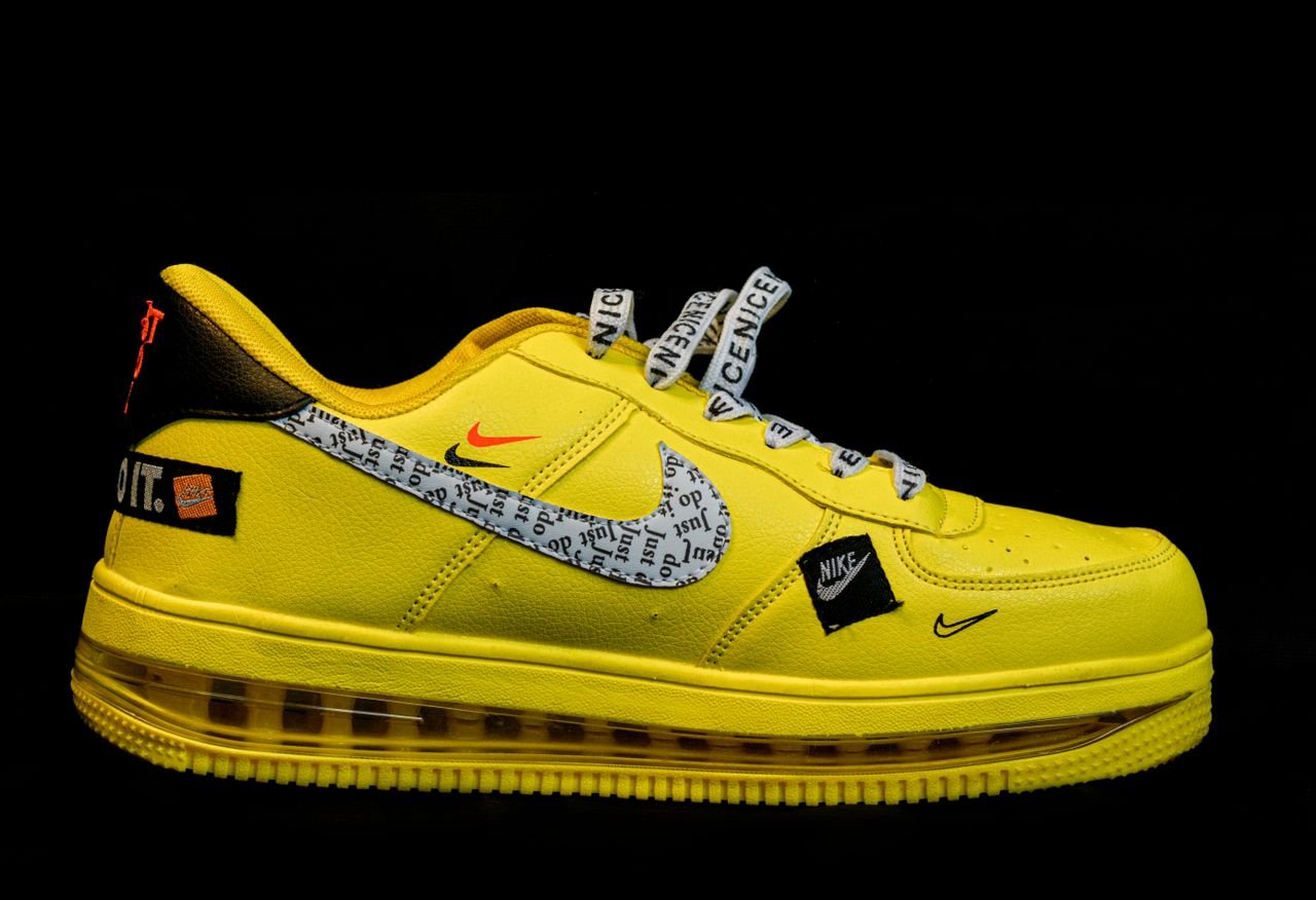 Bright yellow athletic sneaker with text patterns on Nike swoosh, isolated on black background.
