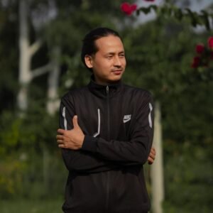 Man in black Nike sportswear posing in a green outdoor setting with flowers.